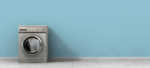A front view of an empty regular brushed metal washing machine in an empty room with a shiny tiled floor and a baby blue wall