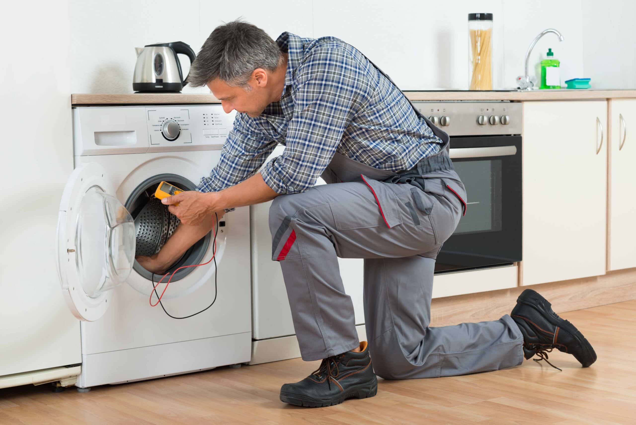 Full length of repairman checking washing machine with digital multimeter at home